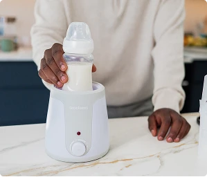 Person placing a baby feeding bottle into a Snookums bottle warmer